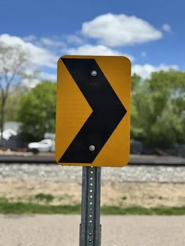 Yellow rectangular sign with a large black chevron arrow marking a curve