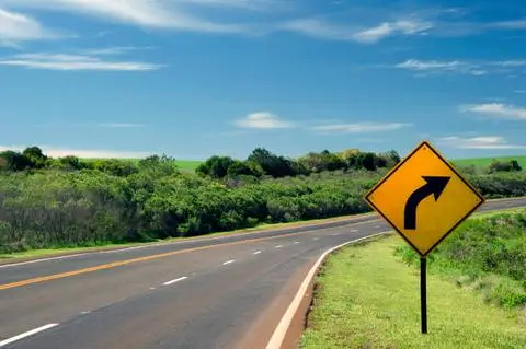 Yellow diamond sign with an arrow curving to the right, beside a rural highway