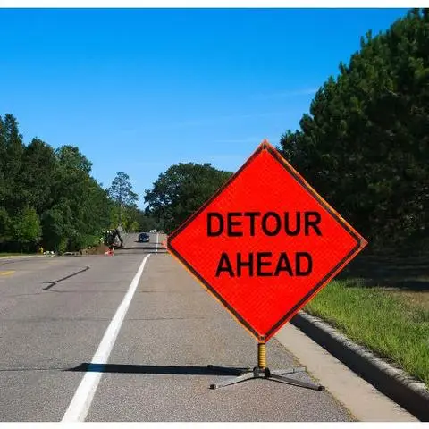 Orange diamond sign reading DETOUR AHEAD on a rural road