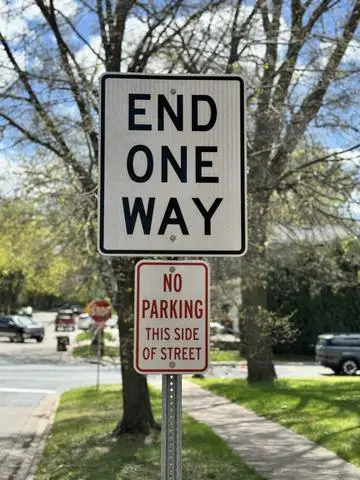 White sign reading END ONE WAY above a NO PARKING THIS SIDE OF STREET plaque