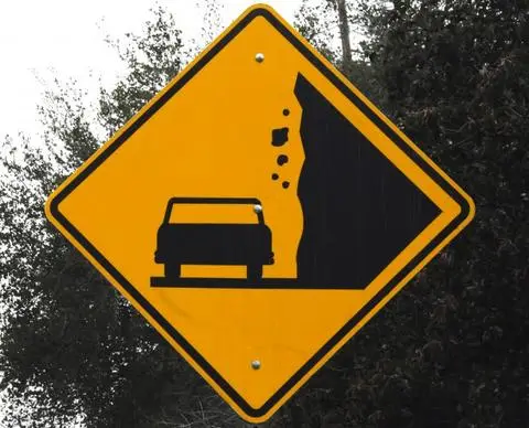 Yellow diamond sign showing boulders falling from a cliff toward a car