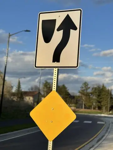 White sign showing a black arrow curving around an obstruction, above a blank yellow diamond