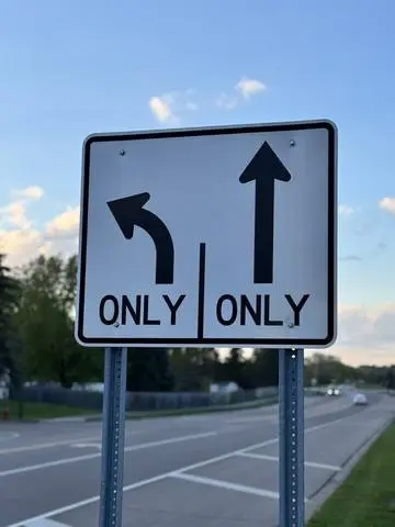 White lane-use sign showing a left-turn arrow marked ONLY beside a straight arrow marked ONLY