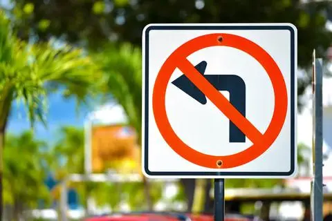 White sign showing a left-turn arrow crossed by a red circle and slash