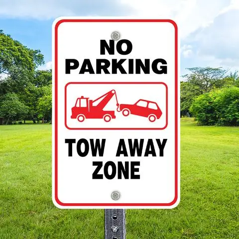 White sign reading NO PARKING with a tow truck symbol and TOW AWAY ZONE