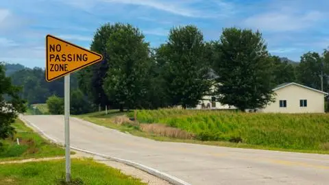 Yellow pennant-shaped NO PASSING ZONE sign on the left side of a two-lane highway