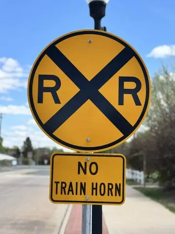 Round yellow railroad advance warning sign with RXR, above a NO TRAIN HORN plaque