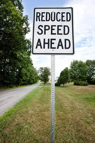 White sign reading REDUCED SPEED AHEAD on a quiet road