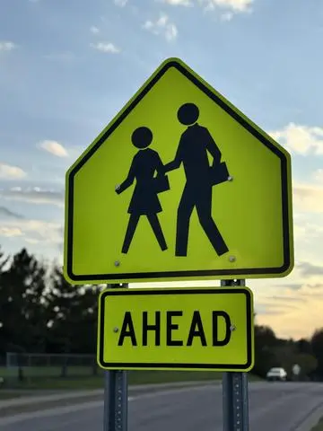 Fluorescent yellow-green diamond sign showing two students walking, with an AHEAD plaque