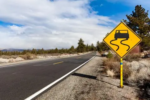 Yellow diamond sign showing a car with wavy skid lines beneath it, beside a rural road