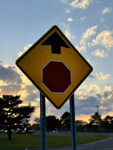 Yellow diamond warning sign showing an arrow pointing to a red octagon, at dusk