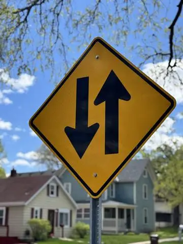 Yellow diamond sign showing two opposing vertical arrows for two-way traffic