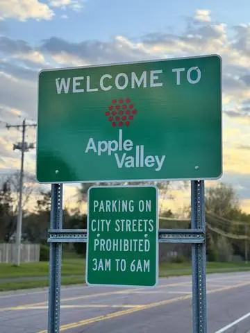 Green WELCOME TO Apple Valley city sign with a plaque prohibiting street parking from 3am to 6am