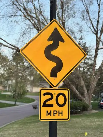 Yellow diamond sign with a winding S-shaped arrow above a 20 MPH advisory plaque