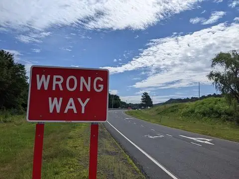 Red WRONG WAY sign facing an empty two-lane road